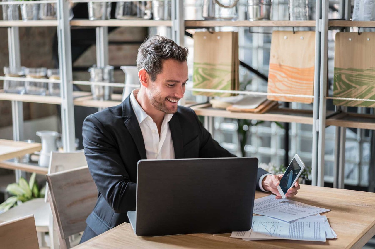 Happy business man working at a restaurant using a laptop computer and smiling